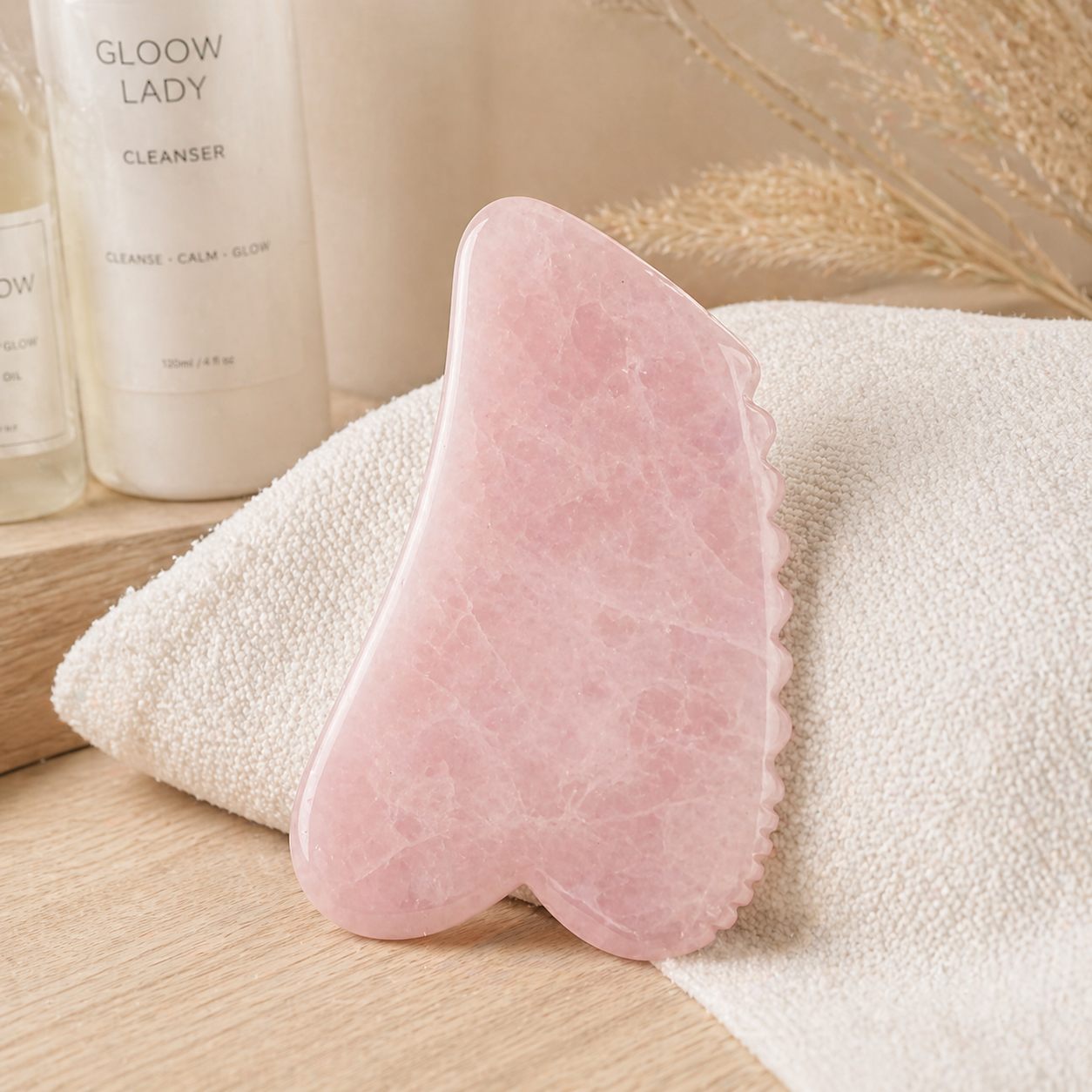 Pink gua sha tool on a towel with 'Glow Lady' cleanser in the background