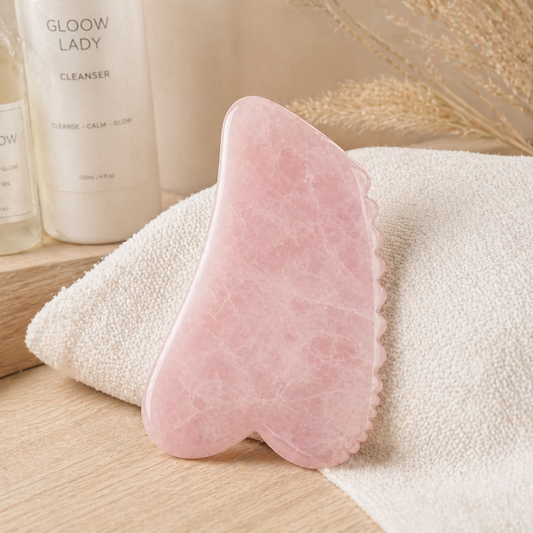 Pink gua sha tool on a towel with 'Glow Lady' cleanser in the background